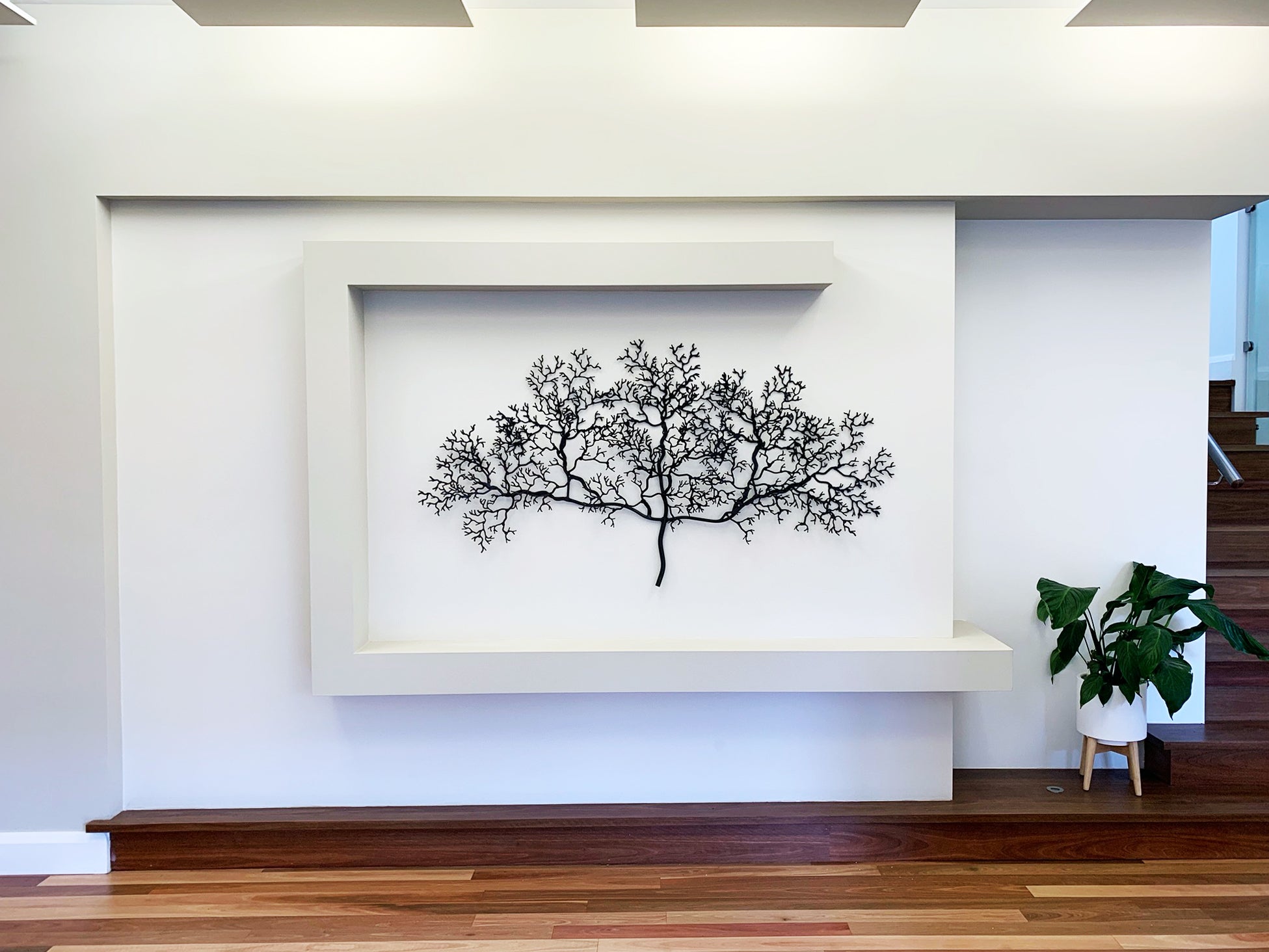 Metal branch design wall art displayed on a white rendered entry wall.